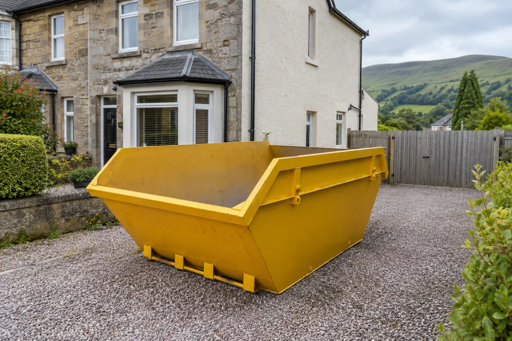 Empty yellow skip on private ground beside a house