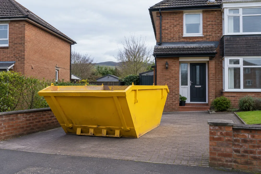 Yellow skip on a paved driveway beside a brick house