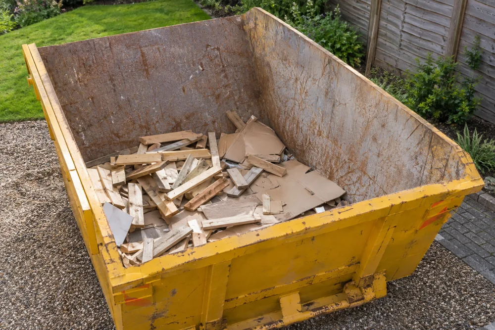 Short timber pieces and flat cardboard well below the rim of a small yellow skip