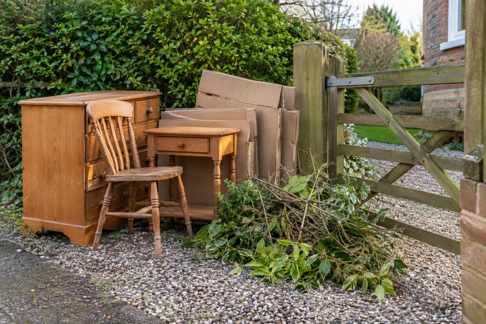 Wooden furniture, cardboard and garden prunings grouped beside a clear garden gate